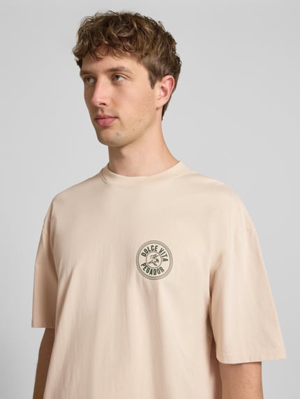 Männermodel trägt Oversized T-Shirt mit Label-Print von Pegador, Beige, Reine Baumwolle, Rundhalsausschnitt, Nahaufnahme Oberkörper.