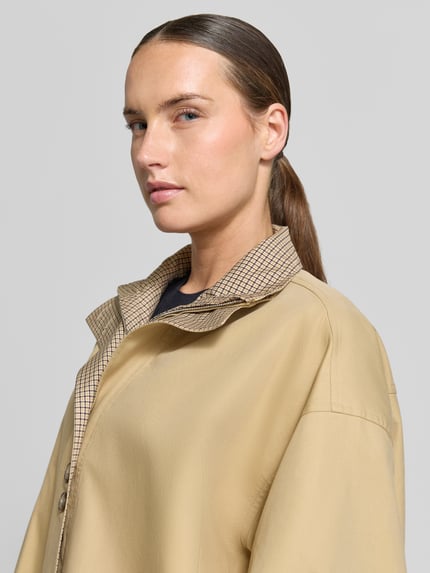 Kobieta modelka nosi Relaxed Fit Jacke mit Lyocell-Anteil od Rich & Royal, mieszanka bawełny i lyocellu, beżowa, stójka, widoczne guziki, plisa, zamek błyskawiczny na całej długości, Długość tyłu w rozmiarze 36: 58 cm, Szerokość ramion w rozmiarze 36: 60 cm, Szerokość klatki piersiowej w rozmiarze 36: 67 cm, Długość rękawów w rozmiarze 36: 54 cm, zbliżenie na górną część ciała z przodu