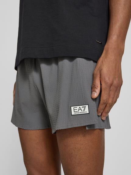 Männermodel trägt Relaxed Fit Shorts mit integriertem Slip von EA7 Emporio Armani, Strukturmuster, Logo-Patch, Elastischer-Material-Mix, Nahaufnahme Oberschenkel.