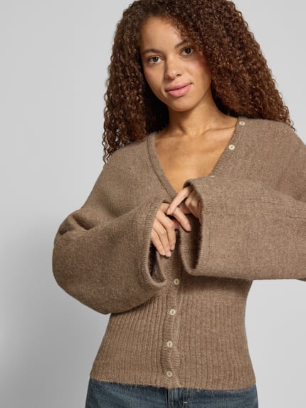 Vrouwenmodel draagt Regular Fit gebreid jack met wol van Gina Tricot, elastische materiaalmix, ribboorden, knoopsluiting, Met lange mouwen, bruine tinten, zichtbare textuur, nahaufnahme bovenlichaam