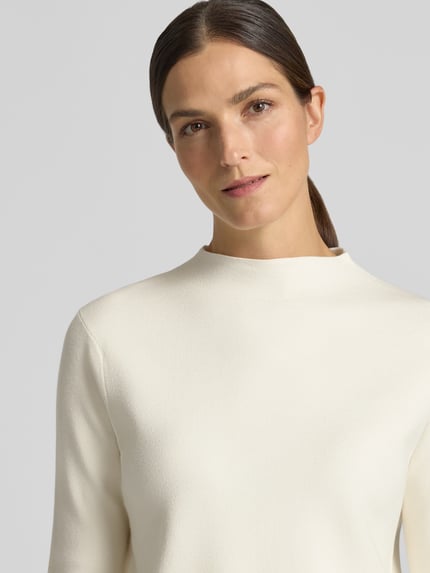 Frauenmodel trägt Strickpullover aus Viskose-Mix Modell 'CHIMNEY' von MANGO in Cremeweiß, glatte Textur, Nahaufnahme Oberkörper, Regular Fit, Stehkragen.