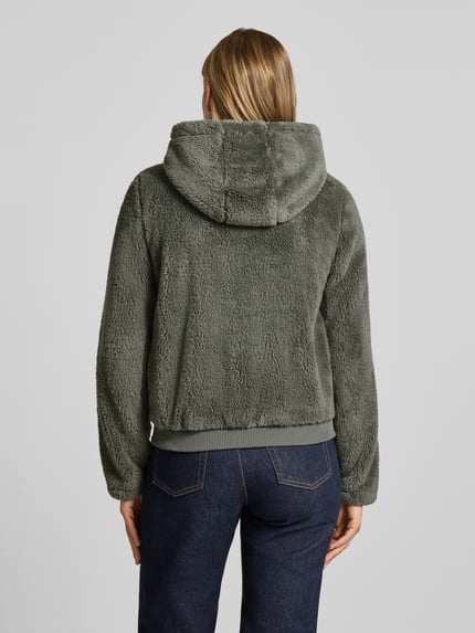 Frauenmodel trägt Regular Fit Teddyjacke mit Kapuze Modell 'NEWANNA' von ONLY in Grün, weiche Plüschtextur, Ganzkörperansicht Rückansicht, Damen Sweatjacke von ONLY.
