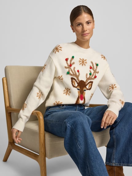 Frauenmodel trägt Strickpullover mit Motiv und Rundhalsausschnitt von Christian Berg Woman, creme mit Rentier und Bommeln, Material-Mix, Regular Fit, Nahaufnahme Oberkörper.