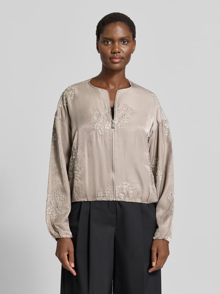 Frauenmodel trägt Blouson aus Viskose-Mix mit Motiv-Stitching Modell 'Ta44mika' von ZABAIONE, beige mit Zierperlen, Ganzkörperansicht von vorne.