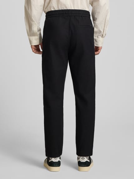 Mannenmodel draagt Tapered Leinenhose aus Baumwoll-Leinen-Mix Modell 'LINUS' van Only & Sons in melange look met elastische tailleband, steekzakken en achterzakken, materiaal katoen-linnenmix, kleuren zwart en crème, achteraanzicht gehele lichaam.