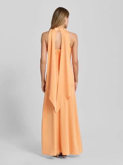 Frauenmodel trägt Neckholder-Maxikleid mit rückseitigem Reißverschluss von Lipsy, Material-Mix mit Stretch-Anteil, Figurbetont, Ganzkörperansicht Rückansicht. Rückenlänge Größe 36: 149 cm, Brustweite: 41 cm. Dezentes Orange, glatte Textur, fließende Form.