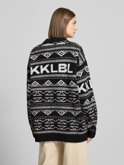 Modelka nosi Jacquard-Strickpullover mit Rundhalsausschnitt von Karo Kauer, czarno-białe wzory, relaxed fit, detal z logo, widok z tyłu, całopostaciowy.
