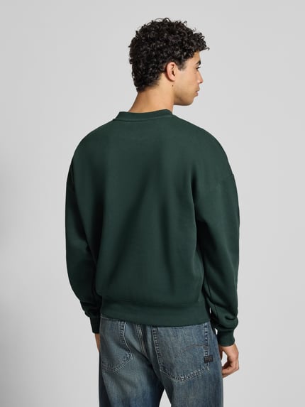 Männermodel trägt Oversized Sweatshirt mit Label-Detail von PROHIBITED in Dunkelgrün aus Baumwoll-Mix, Gerippte-Abschlüsse, Rückenlänge 68 cm, Ärmellänge 70 cm, Ganzkörperansicht Rückansicht.