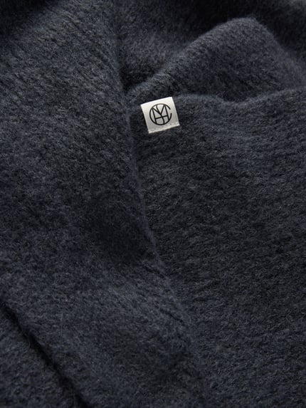 Produktfoto, Schal aus elastischem Woll-Mix mit Alpaka-Anteil Modell 'Hope' von MSCH Copenhagen, dunkelgraue Farbe, weich strukturierte Oberfläche, rechteckige Form, Label-Detail sichtbar, Breite 41 cm, Länge 105 cm.