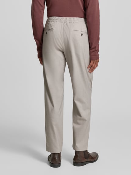 Männermodel trägt Stoffhose mit elastischem Bund von MCNEAL in Beige, Gesäßtaschen, lockerer Schnitt, Ganzkörperansicht Rückansicht.