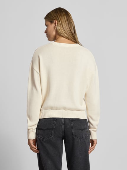Frauenmodel trägt Strickpullover aus reiner Baumwolle von REVIEW in Creme mit lockerer Passform und gerippten Abschlüssen, Ganzkörperansicht Rückansicht.