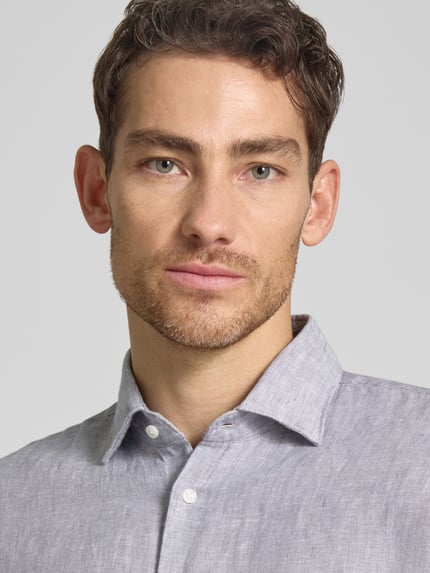 Männermodel trägt Slim Fit Business-Hemd aus Leinen mit Kentkragen von SEIDENSTICKER, reine Leinen, Nahaufnahme Oberkörper. Rückenlänge bei Größe 40: 69 cm, Schulterbreite: 43 cm, Ärmellänge: 64 cm, Knopfleiste, hellgraue Farbe, feine Leinenstruktur.
