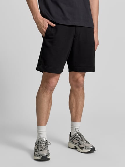 Männermodel trägt schwarze Regular Fit Sweatshorts aus Baumwoll-Mix Modell 'JT_SHORTS' von BOSS Green, Ganzkörperansicht von vorne.
