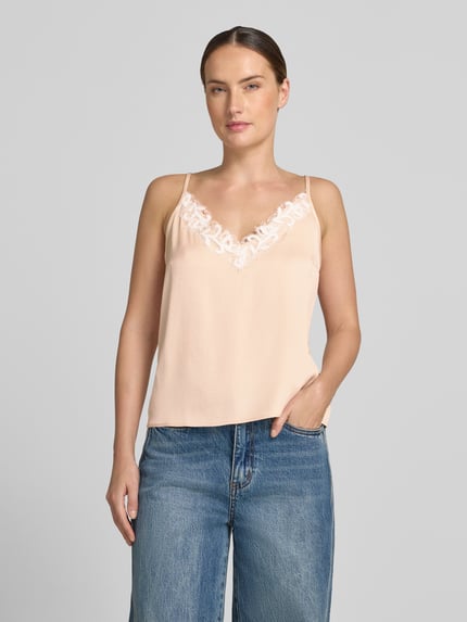 Frauenmodel trägt Blusentop mit obszyciem koronką Modell 'GIONA' von DRYKORN, mieszanka materiałów z dodatkiem streczu, krój regular fit, cienkie ramiączka, dekolt w serek, długość tyłu w rozmiarze 36: 33 cm, kolor jasnobeżowy, gładka tekstura, Ganzkörperansicht von vorne.