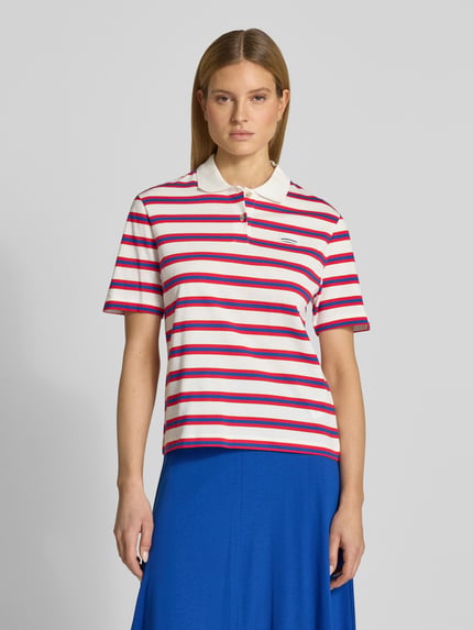 Frauenmodel trägt Loose Fit Poloshirt aus reiner Baumwolle Modell 'STRIPE POLO' von Armedangels, Optik: Unifarben, Mehrfarbig, Gestreift, Passform: Loose-Fit, Muster: Gestreift, Label-Stitching-Applikation, Polokragen, V-Ausschnitt, kurze Knopfleiste, Ärmelform: Kurzarm, Materialverarbeitung: Feinripp, Material: Reine Baumwolle, Ganzkörperansicht von vorne.