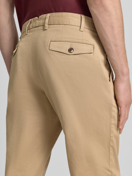 Mężczyzna nosi chinosy Chino mit Eingrifftaschen von Christian Berg Men z mieszanki bawełny i elastanu, krój regular fit, beżowe, widok z tyłu, detal z wpuszczanymi kieszeniami i kieszenią z tyłu, szerokość w rozmiarze 50: 43 cm, długość wewnętrzna nogawki w rozmiarze 50: 82 cm, tekstura gładka. Zbliżenie tylnej części.