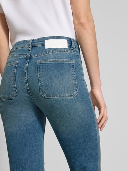 Frauenmodel trägt Flared Jeans mit Knopfverschluss von OPUS, blauer Baumwoll-Mix, sichtbare Gesäßtaschen, Ganzkörperansicht Rückansicht.