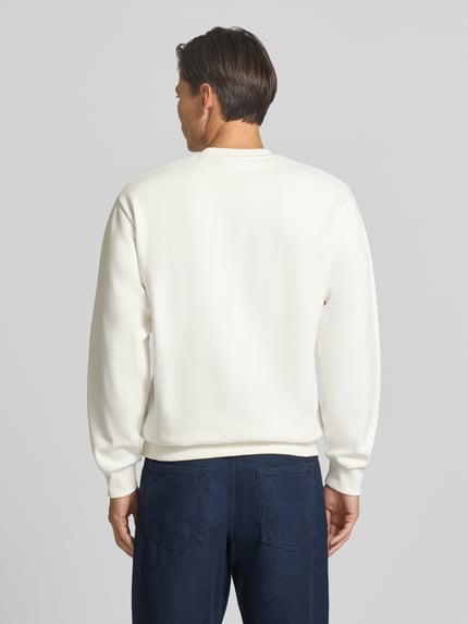 Męski model nosi Regular Fit Sweatshirt aus Baumwoll-Mix von Lacoste, gładka biała tkanina, ciemnoniebieskie spodnie, Ganzkörperansicht Rückansicht.