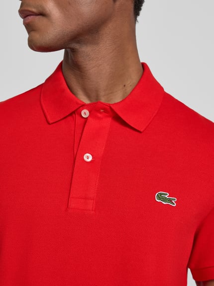 Mężczyznamodel nosi Slim Fit Poloshirt aus reiner Baumwolle von Lacoste w kolorze intensywnej czerwieni, tekstura pikowana, zbliżenie na górną część ciała