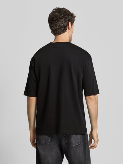 Männermodel trägt Loose Fit T-Shirt aus reiner Baumwolle von Dsquared2, schwarz, Halbarm, verlängerte Rückseite, Ganzkörperansicht Rückansicht.
