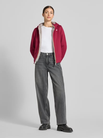 Frauenmodel trägt Sweatjacke mit Futter aus Kunstfell und Zweiwege-Reißverschluss von K-WAY, rot mit weißem Innenfutter, Regular Fit, Strech-Materialmix, Kapuze, Logo auf der Brust, kombiniert mit grauer Jeans, glatte Textur, Ganzkörperansicht von vorne.