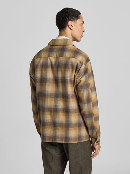 Männermodel trägt Regular Fit Overshirt aus Woll-Mix von Forét, kariertes Muster in Beige und Braun, Rückenansicht, Ganzkörperansicht Rückansicht. Rückenlänge 71 cm, Schulterbreite 47 cm, Ärmellänge 67 cm, Umlegekragen, Reißverschluss, Eingrifftaschen.