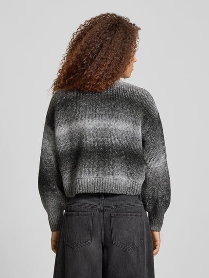 Frauenmodel trägt Cardigan mit überschnittenen Schultern Modell 'ORADEA' von Pegador, Relaxed-Fit, Rundhalsausschnitt, Knopfleiste, Rückenlänge 46 cm bei Größe S, Ärmellänge 51 cm bei Größe S, Farbe Grau-Schwarz mit Farbverlauf, grob gestrickte Textur, Ganzkörperansicht Rückansicht.