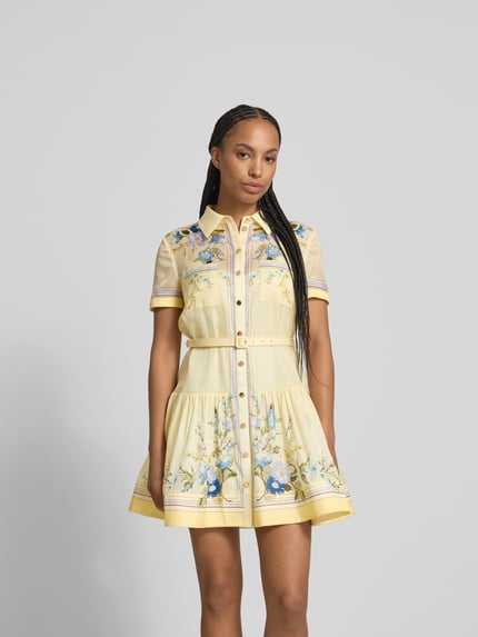 Frauenmodel trägt Minikleid mit Seide-Anteil von Self-Portrait, gelb mit floralen Mustern, tailliert, Brusttaschen, Gürtel, Nahaufnahme Oberkörper.