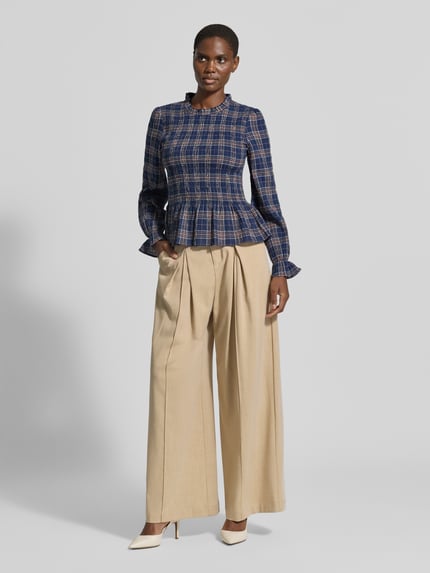 Frauenmodel trägt Bluse mit Smok-Details und Rüschenärmeln von Christian Berg Woman Selection, taillierter Schnitt, Rundhalsausschnitt, Baumwoll-Mix mit Stretch-Anteil, Rüschen, langen Ärmeln, kariertes Muster in Blau, Beige-Ton bei Hose, Ganzkörperansicht von vorne.