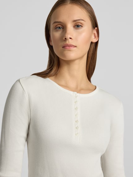 Frauenmodel trägt Slim Fit Langarmshirt aus reiner Baumwolle von REVIEW, weiß, Rippenstruktur, Knopfleiste, Nahaufnahme Oberkörper.