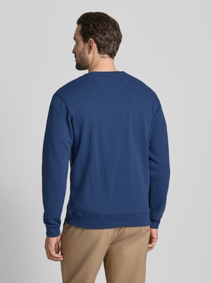 Männermodel trägt Sweatshirt mit Label-Detail von Scotch & Soda, reine Baumwolle, lockerer Schnitt, gerippte Abschlüsse, Ganzkörperansicht Rückansicht.