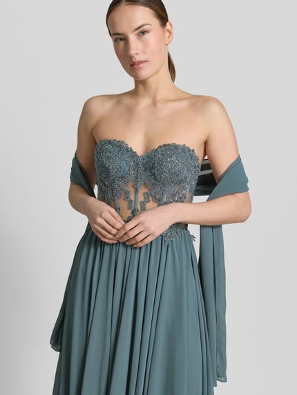 Frauenmodel trägt Abendkleid mit Spitze und Gehschlitz von Mascara in Tailliertem Schnitt, Maxilänge, semitransparenter Spitze, Strasssteinbesatz; Nahaufnahme Oberkörper.