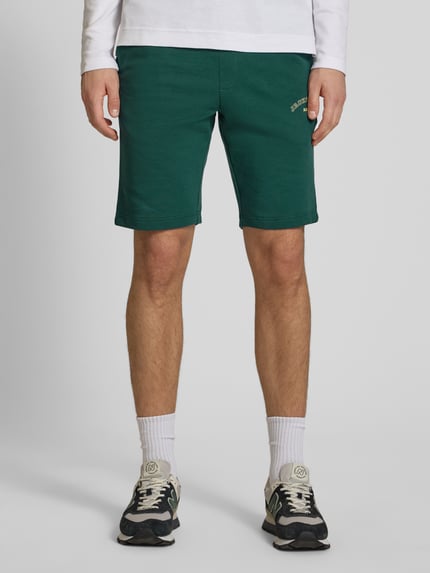 Männermodel trägt Shorts mit Logo-Print Modell 'GORDON' von Jack & Jones aus grünem Baumwoll-Mix, Relaxed-Fit, Nahaufnahme Oberschenkel frontal.
