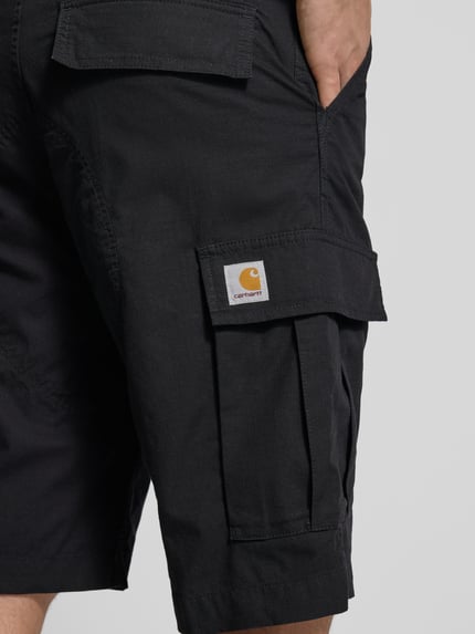 Männermodel trägt schwarze Shorts mit Cargotaschen von Carhartt Work In Progress, robuste Struktur, Nahaufnahme Oberschenkel, Regular Fit.