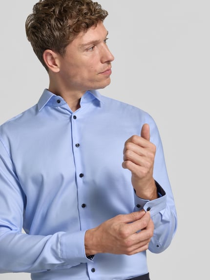 Männermodel trägt Regular Fit Businesshemd mit kontrastierendem Innenkragen von Seidensticker in Hellblau mit Kentkragen und dunklen Knöpfen, feines Webmuster, Nahaufnahme Oberkörper.
