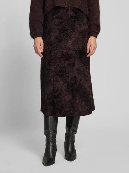 Frauenmodel trägt Midirock im Allover-Look Modell 'SESSOLANA' von FREE/QUENT, dunkle Farben, strukturierte Oberfläche, Nahaufnahme Unterkörper, Material-Mix mit Stretch-Anteil, gerader Schnitt, KI-modifiziertes Bild.