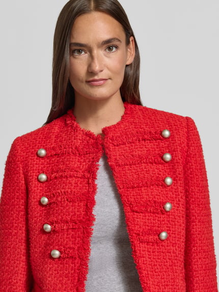 Frauenmodel trägt Blazer in Bouclé-Optik Modell 'CAROLINA' von MANGO in Rot, Zierknöpfe, Fransensaum, Baumwoll-Mix, Nahaufnahme Oberkörper.