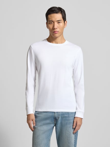 Männermodel trägt Longsleeve mit gerippten Abschlüssen von Scotch & Soda in Weiß, Regular-Fit, reine Baumwolle, Rundhalsausschnitt, Ganzkörperansicht von vorne. Rückenlänge bei Größe M: 65 cm.
