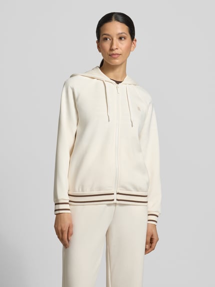 Frauenmodel trägt Regular Fit Sweatjacke aus Viskose-Mix mit Logo-Stitching von ARMANI EXCHANGE in Beige mit Reißverschluss, Kapuze und elastischen Abschlüssen, Ganzkörperansicht von vorne.