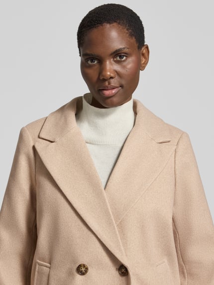 Frauenmodel trägt Mantel mit abnehmbarer Kapuze Modell 'VMGRACE' von VERO MODA in Beige, strukturierte Webware, Zierknöpfe, Nahaufnahme Oberkörper.