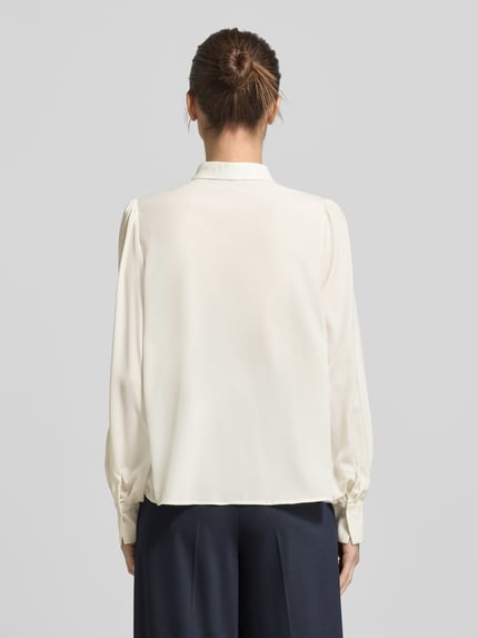 Frauenmodel trägt Regular Fit Bluse mit Bubikragen von Christian Berg Woman Selection in Creme, mit Falten, Knopfleiste und Schnürung, Rückenlänge 60 cm, Ärmel 65 cm, Ganzkörperansicht Rückansicht.