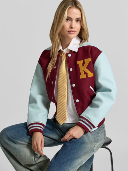 Frauenmodel trägt College-Jacke mit Logo-Patch von Kenzo in Two-Tone-Optik mit Strukturmuster, Kontraststreifen und Druckknöpfen, Nahaufnahme Oberkörper.