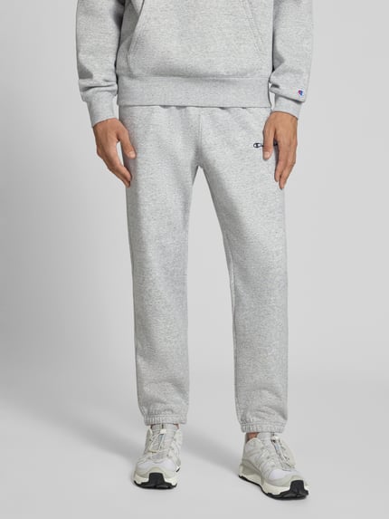 Männermodel trägt Sweatpants mit Label-Stitching Modell 'ICONS' van Champion in lichtgrijs katoenmix, steekzakken, recht model, elastische band, binnenbeenlengte maat M 76 cm, Ganzkörperansicht von vorne