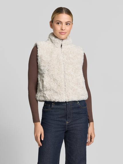 Kobiece modelka nosi Regular Fit Weste aus Kunstfell mit Stehkragen od monari, jasny beż, zamek błyskawiczny, sztuczne futro, krój regular fit, stójka, Długość tyłu w rozmiarze 36: 47 cm, Szerokość ramion w rozmiarze 36: 39 cm, Szerokość klatki piersiowej w rozmiarze 36: 45 cm, Ganzkörperansicht z przodu.