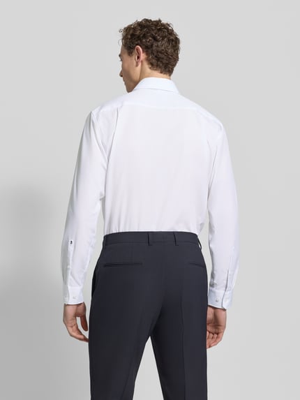 Männermodel trägt Regular Fit Business-Hemd mit Kentkragen von SEIDENSTICKER aus reiner Baumwolle, weiß, glatte Textur, Ganzkörperansicht Rückansicht.