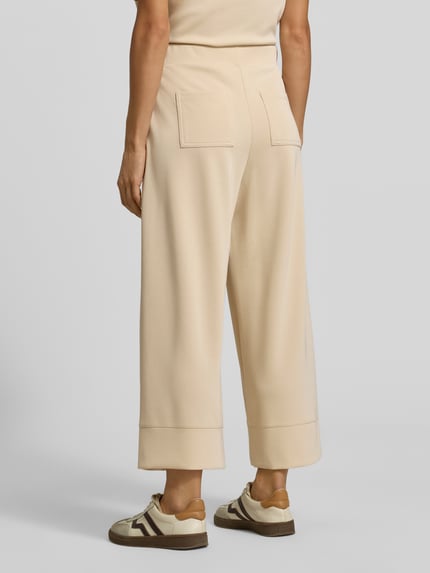 Frauenmodel trägt Wide Leg Sweatpants aus Modal-Mix von Rich & Royal in Beige mit Bundfalten, seitlichen Eingrifftaschen, Gesäßtaschen, Ganzkörperansicht Rückansicht.