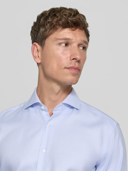 Männermodel trägt Regular Fit Businesshemd mit Kentkragen von BOSS in Hellblau, feines Webmuster, Nahaufnahme Oberkörper.