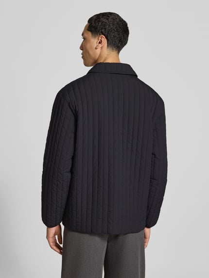 Männermodel trägt kurtka pikowana 'Steppjacke mit Brusttasche' von MAISON KITSUNÉ, czarny kolor, prosty krój, Ganzkörperansicht Rückansicht. Długość tyłu w rozmiarze M: 67 cm, szerokość w rozmiarze M: 47 cm, długość rękawów w rozmiarze M: 62 cm, listwa z zatrzaskami, brustasza, wpuszczane kieszenie, detal z logo, elastyczne zakończenia rękawów.