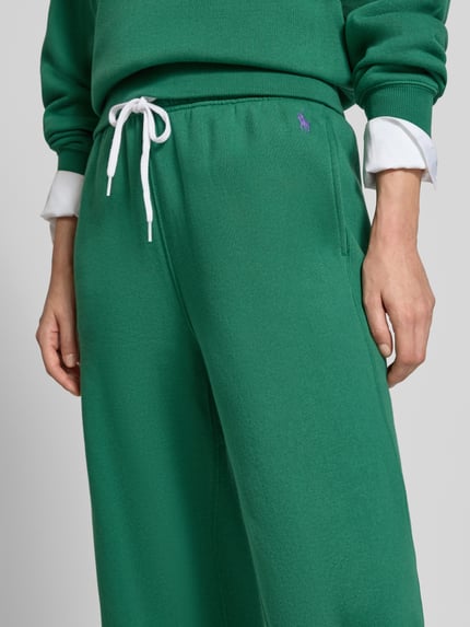 Kobieta nosi zielone spodnie Wide Leg Sweathose aus Baumwoll-Mix mit Logo-Stitching od Polo Ralph Lauren, damskie spodnie, zbliżenie na biodra.