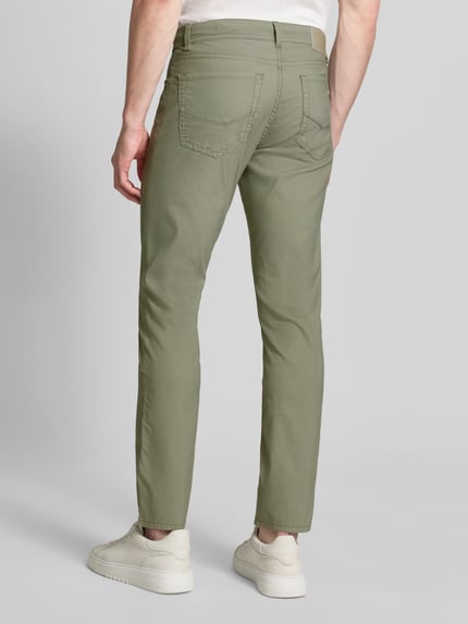 Mężczyzna model nosi Regular Fit Hose mit Label-Detail Modell 'Lyon' von Pierre Cardin, mieszanka bawełny z dodatkiem streczu, krój regular fit, drobno fakturowane, detal z logo, szerokość w rozmiarze 32/32: 43 cm, długość wewnętrzna nogawki: 79 cm, spodnie zielone, całkowity widok z tyłu.